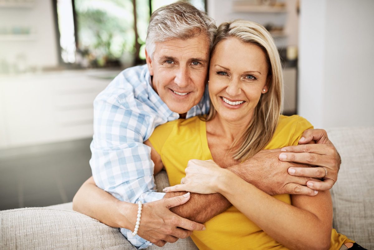 Happy, in love and affectionate senior couple hugging on the sofa in the living at room, enjoying time together and their retirement. Portrait of a happy man and woman bonding and smiling at home.